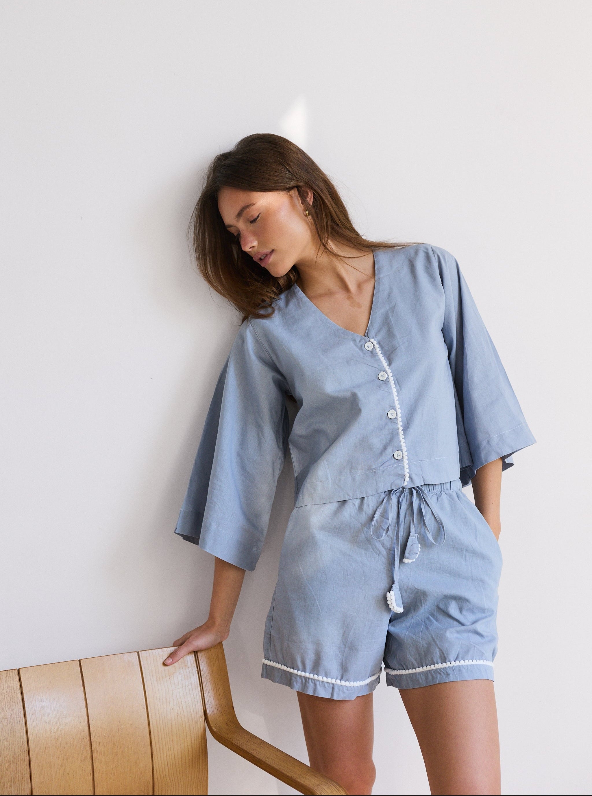 Woman wearing a light blue pajama set against a white wall.